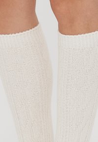Knee-length cream socks with a textured ribbed design and zigzag pattern, featuring a wavy top edge and a smooth knit finish.