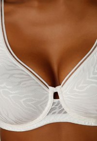 Hvid blonde bh med et subtilt bølgemønster, der har tynde stropper, en nøglehulldetalje i midten og et struktureret underbånd.