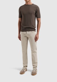 Bruine geribbelde trui met korte mouwen gecombineerd met beige op maat gemaakte broek en bruine sneakers met witte accenten en veters.