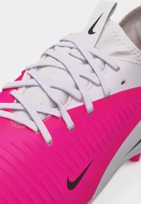 Λευκό και ροζ παπούτσι ποδοσφαίρου της Nike με λευκά κορδόνια, που έχει μαύρα λογότυπα Nike στο γλώσσα και στην πλευρά του παπουτσιού.