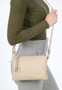 Borsa a tracolla in pelle beige con finitura testurizzata, tracolla regolabile e accessori in argento. Presenta una chiusura con zip e logo impresso.