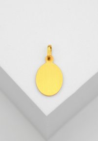 Pendentif ovale en or avec une petite boucle en haut, présenté sur une surface géométrique blanche.