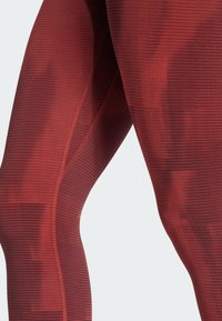 Rød teksturerede leggings med et geometrisk mønster, fremstillet af strækbart materiale, der viser en tætsiddende design og sømløs konstruktion.
