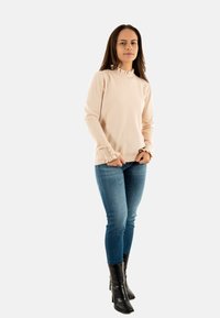 Lichtroze langemouwensweater met een gerimpelde halslijn en knoopmanchetten, gecombineerd met blauwe skinny jeans en zwarte hoge hakken.