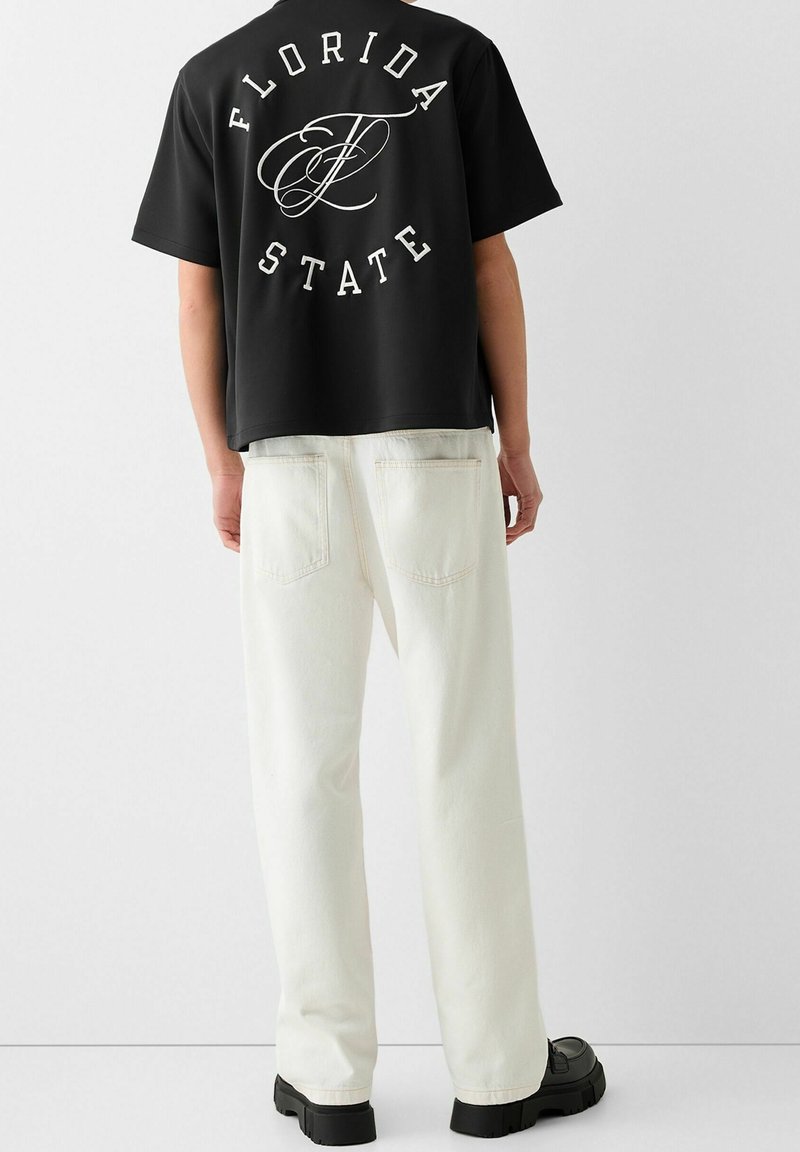 Czarny t-shirt z krótkim rękawem z białym napisem "FLORIDA STATE" na plecach, zestawiony z białymi luźnymi jeansami i czarnymi butami.