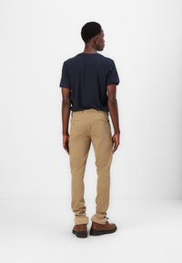 Brown ankle boots, khaki trousers, and a navy t-shirt. The outfit features a simple design with a relaxed fit and smooth texture.