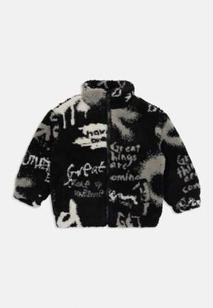 Giacca in pile nera e grigia con cerniera frontale completa, collo alto, polsini elastici e motivi di testo bianco in stile graffiti astratto.