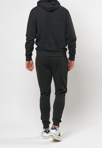 Black cotton hoodie with a kangaroo pocket, ribbed cuffs, and a drawstring hood, paired with black tapered joggers and white sneakers.