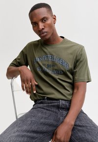 Olivengrøn bomulds t-shirt med korte ærmer, med en mørkeblå tekstgrafik, der siger "JEANS INTELLIGENCE EST. 90 DIV. BY JACK & JONES."