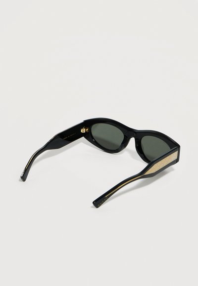Γυαλιά ηλίου με μαύρους φακούς σε σχήμα γάτας, χρυσές λεπτομέρειες στα πλευρά και το λογότυπο της Gucci στις άκρες των βραχιόνων.