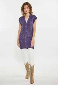 Vest tricotat violet cu un model texturat și nasturi din lemn, asortat cu pantaloni albi și bocanci de cowboy bej.