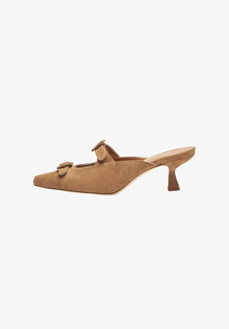 Mules de ante marrón con punta afilada, dos bucles decorativos en la parte superior y un tacón delgado y angular. Textura suave y diseño minimalista.