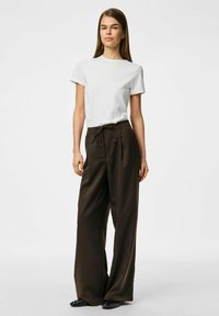 T-shirt blanc à col rond associé à un pantalon marron à rayures fines, taille haute et coupe large ; texture lisse et coupe décontractée. Des chaussures noires complètent le look.