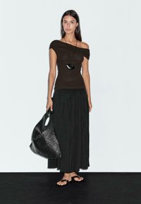 Braunes schulterfreies Oberteil, schwarze plissierte Maxirock, schwarze geflochtene Tote-Tasche und schwarze Sandalen. Minimalistisches Design mit glatten Texturen.