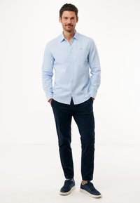 Lichtblauw overhemd met lange mouwen, gecombineerd met slim-fit marineblauwe broeken en donkere sneakers. Bevat een klein logo op het shirt.