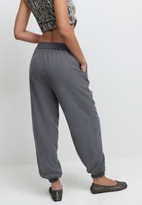 Graue, leichte Jogginghosen mit elastischem Bund, Seitentaschen und gerippten Beinabschlussbündchen. Glatte Textur mit entspanntem Schnitt.