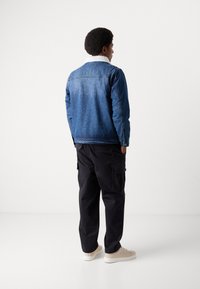 Jeansjacke mit weißem Fellkragen, blauer Farbe und lässiger Passform, kombiniert mit schwarzen Cargo-Hosen und beigen Schuhen.
