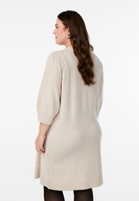 Beige stickad klänning med en avslappnad passform, som har puffärmar och ribbad fåll. Mjuk textur, knälång och med sidsprund för bättre rörelsefrihet.