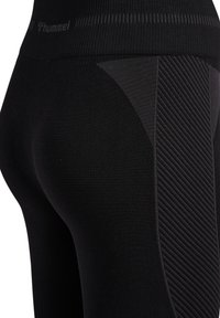 Svarta atletiska leggings med en texturerad design på sidorna, ribbad midja och en slät tygfinish med diskret varumärkning.
