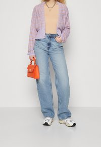 Cardigan en tricot lavande, haut beige, jean large bleu clair, sac à main orange et baskets blanches avec des accents noirs.