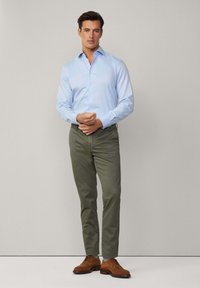 Camicia azzurro chiaro con bottoni, pantaloni verdi e scarpe in pelle marrone. Tessuto liscio con una vestibilità slim, caratterizzata da un colletto classico e maniche lunghe.
