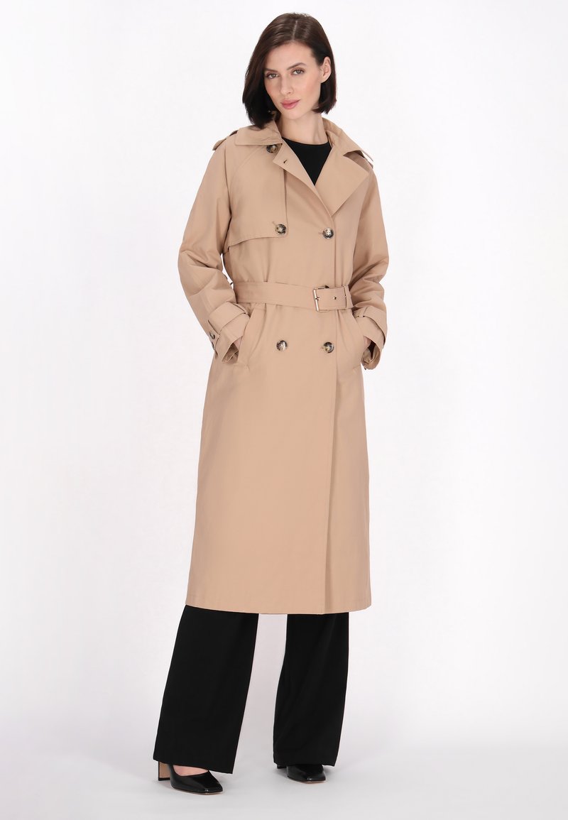 Trench coat bej cu talie centurată, cu un front cu două rânduri de butoane și butoane mari. Are un guler clasic și mâneci lungi.