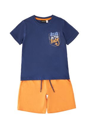 Granatowy t-shirt z krótkim rękawem z napisem „Read on the Back” na kieszeni, zestawiony z jasnopomarańczowymi spodenkami ze sznurkiem.