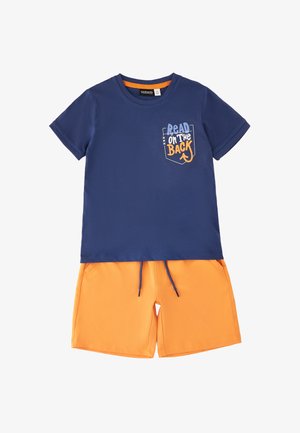 Granatowy t-shirt z krótkim rękawem z napisem „Read on the Back” na kieszeni, zestawiony z jasnopomarańczowymi spodenkami ze sznurkiem.