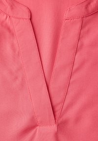 Gros plan sur le col en V en tissu rose avec coutures visibles et détails pliés au niveau de l'encolure.