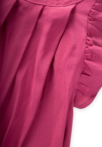 Tessuto rosa con una texture liscia e una leggera lucentezza, caratterizzato da ruffles arricciati lungo la cucitura della spalla e delicate pieghe.