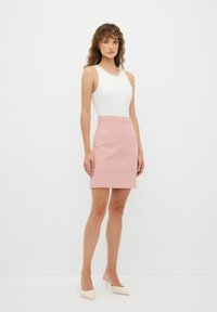 Top blanco sin mangas con un cuello de cuentas, combinado con una falda mini rosa ajustada y tacones de color claro; texturas suaves en toda la prenda.