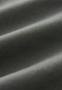 Tessuto grigio con una consistenza liscia, caratterizzato da sottili righe orizzontali e pieghe leggermente ondulate, che riflettono la luce in morbide ombre.