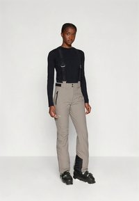 Lehké šedé lyžařské kalhoty s nastavitelnými černými kšandami, kapsami na zip a přiléhavým střihem. Kombinované s černým dlouhým rukávem.