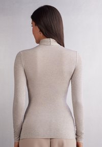 Světle béžová dlouhá turtleneck košile s dlouhým rukávem vyrobená z měkké, strukturované tkaniny s přiléhavým střihem a jemnými švy kolem výstřihu.