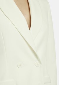 Weißes doppelt geknöpftes Blazer mit tiefem V-Ausschnitt und glattem Stoff. Verfügt über zwei runde Knöpfe und strukturierte Revers.