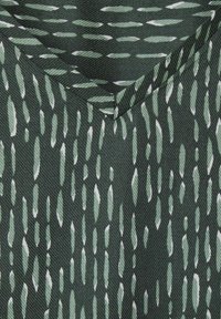 Tessuto verde con una superficie texturizzata, caratterizzato da un motivo verticale di forme allungate bianche e verde chiaro. Dettaglio del design a scollo a V visibile.