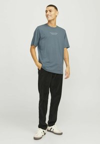 Donkerblauwe katoenen T-shirt met een ronde hals en korte mouwen, voorzien van een subtiele logo-opdruk. Gemaakt in combinatie met zwarte corduroy broek en witte sneakers.