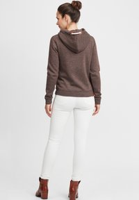 Brun hettegenser med teksturert stoff, som har justerbar hette og trefunksjon. Kombinert med hvite slim-fit jeans og brune ankelstøvler.