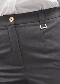 Schwarze maßgeschneiderte Hose mit glatter Textur, ausgestattet mit einem goldfarbenen Knopf und einem kleinen rechteckigen Schlaufenakzent am Bund.