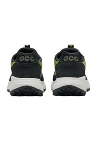 Svarta sneakers med överdel av mesh och mocka, ljusgrön accent, framträdande "acg"-logotyp på hälen och en texturerad, svart gummisula.