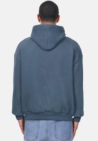 Sweat �à capuche gris foncé, avec une coupe décontractée, des poignets et un ourlet côtelés, et une texture douce. L'arrière présente une capuche centrée.
