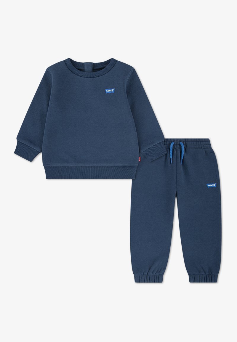 Súprava v námorníckej modrej farbe zahŕňa mikinu a nohavice z jemnej látky. Má rebrované manžety a pás; logo Levi’s v svetlomodrej farbe.