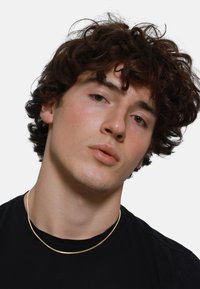 Collier en métal doré au design lisse et plat, porté sur un t-shirt noir. Comprend deux brins courbés entrelacés.