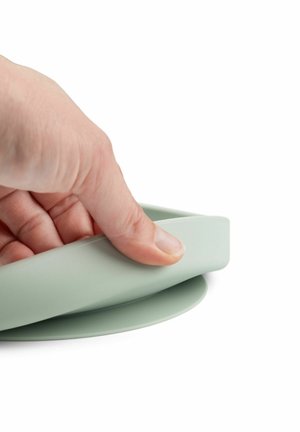 Minkšto žalio silikono dangtelis, spaudžiamas rankos. Dangtelyje yra lygi tekstūra ir apvali, šiek tiek pakelta briauna.