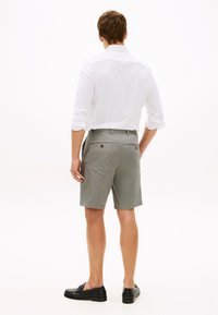 Γκρι βαμβακερά σορτς μέχρι το γόνατο, με δύο πίσω τσέπες και επίπεδη μπροστινή όψη. Συνδυασμένα με λευκό μακρυμάνικο πουκάμισο και μαύρα μοκασίνια.