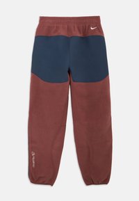 Nike zúžené tepláky v bordovej a námorníckej modrej, s textúrovaným povrchom, elastickým pásom a bočnými logami. Dizajn s kontrastnými farebnými blokmi.