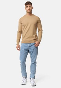 Lys beige strikket sweater med rund hals, parret med lys blå lige ben jeans og hvide sportsko.