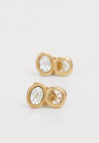 Boucles d'oreilles en métal doré présentant un double design avec des cristaux ovales transparents et un détaillage découpé complexe dans une section.