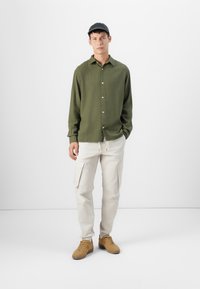 Green button-up shirt, beige cargo pants with side pockets, and brown sneakers. Smooth texture, relaxed fit, and simple design.