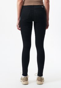 Czarne wąskie dżinsy o dopasowanym kroju, z talią średniego wzrostu i tylnymi kieszeniami. Materiał wydaje się gładki i elastyczny, w połączeniu z beżowymi sneakersami.